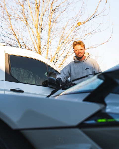 Man standing by open car door with bare tree branches in background