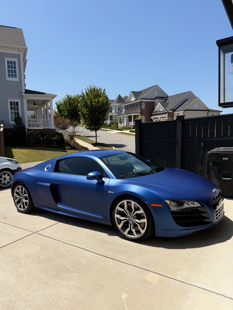 Blue Audi R8 sports car parked in driveway of suburban home on clear day