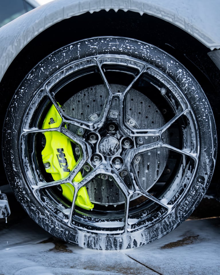 Close-up of a wet car wheel with bright neon yellow brake calipers and chrome alloy rim